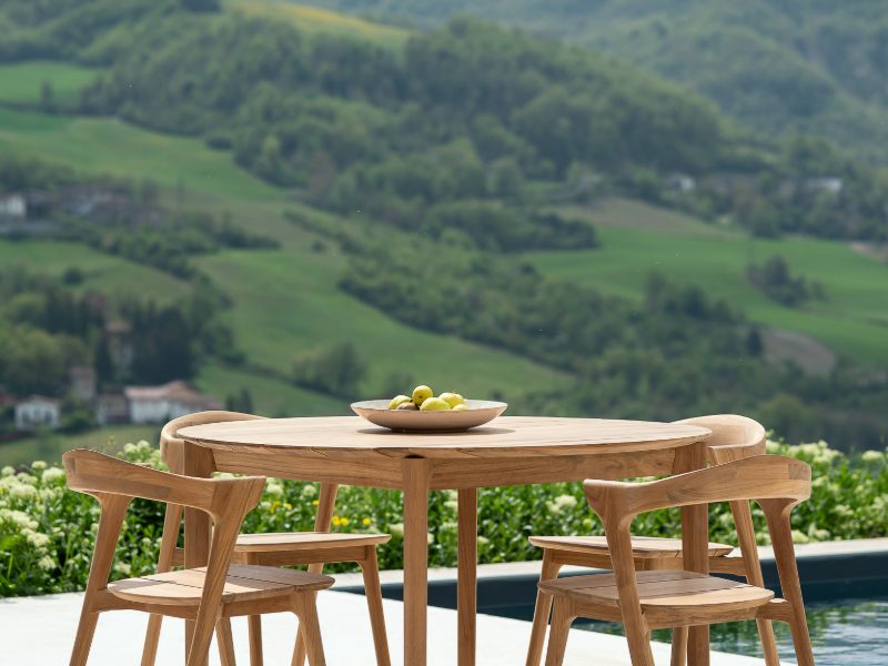 An outdoor dining table and chairs in teak overlooking a valley