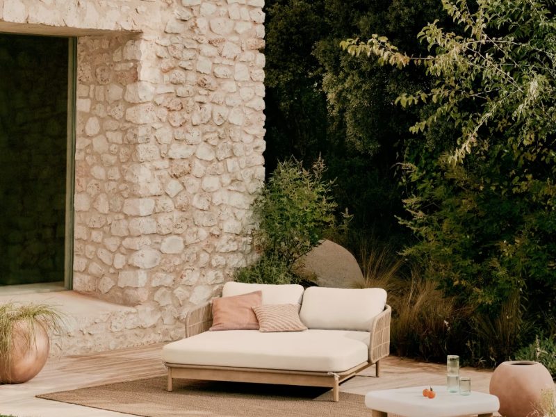 An outdoor daybed beside a pool against a stone wall